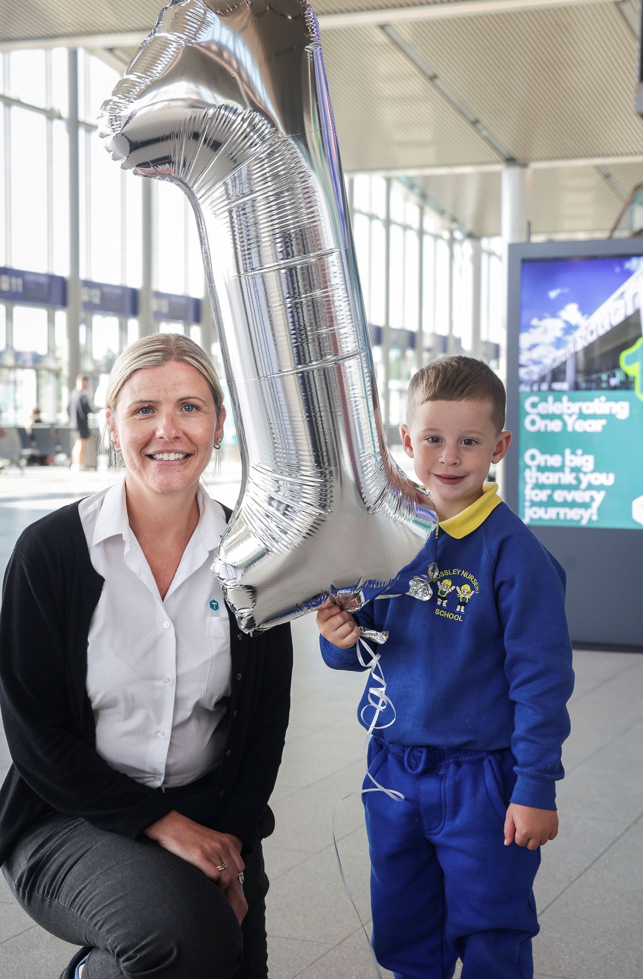 A photo of two people holding a balloon in the shape of a number one at Belfast Grand Central Station
