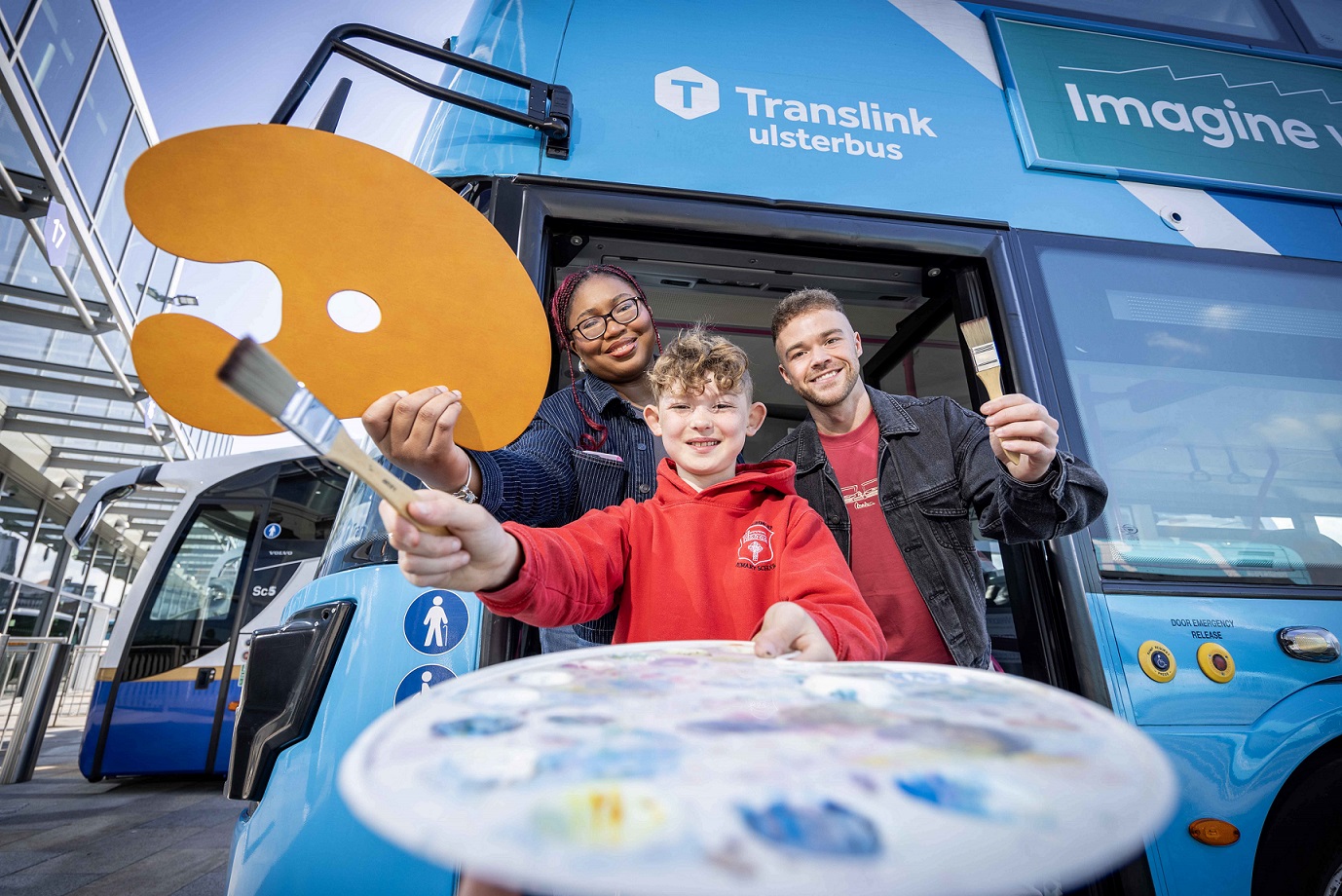 A photo of a young boy in front of a Translink bus, holding an artist's pallet