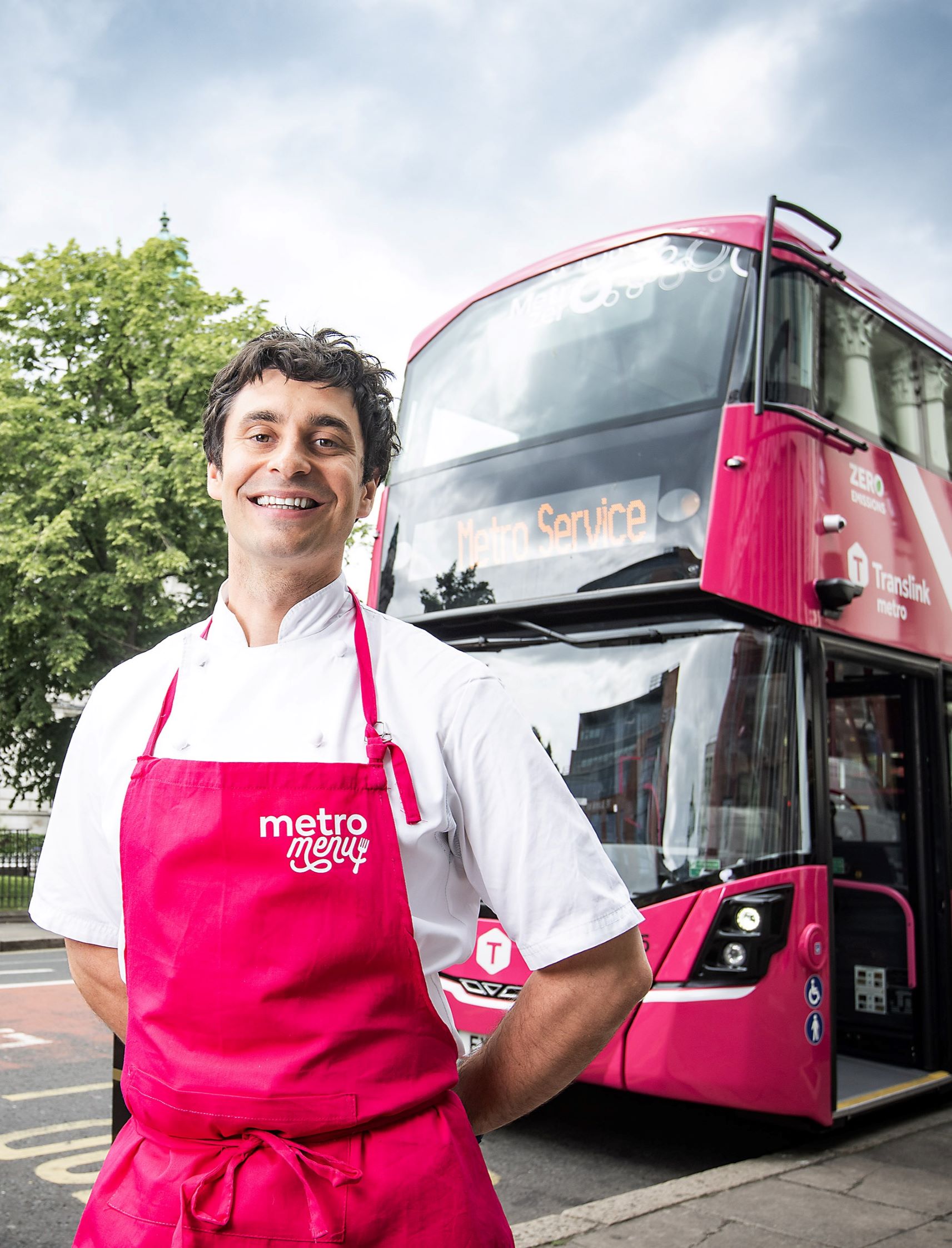 Photo of award-winning chef, and Metro Menu guest judge, Chris McClurg standing with a Belfast Metro bus