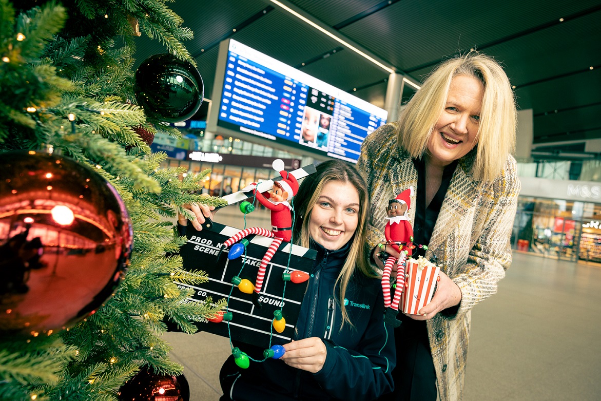Two women holding Christmas decorations and popcorn next to a Christmas tree in Belfast Grand Central Station
