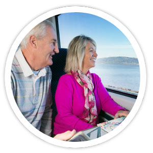 Two Senior SmartPass users are sitting onboard a train, looking out the window at a coastal view